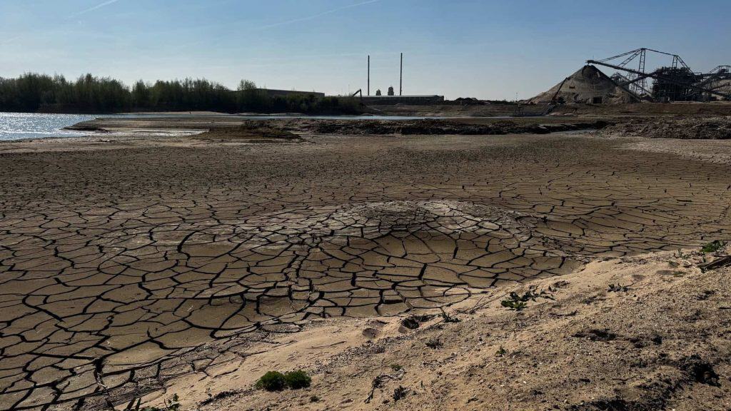 Drooggevallen rivierbedding op 't Gelders Eiland met krakende aarde en industriële achtergrond.