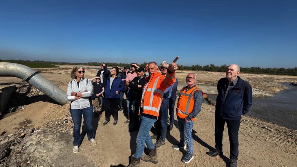 Groepsbezoek op 't Gelders Eiland met gids en bouwers in open landschap onder blauwe hemel.