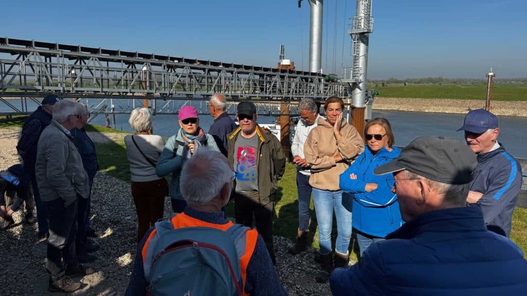 Kleine groep mensen op excursie bij 't Gelders Eiland, met industriële achtergrond en heldere blauwe.