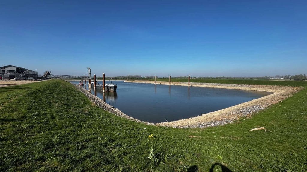 Zicht op 't Gelders Eiland met water en groene oevers onder een heldere blauwe hemel.