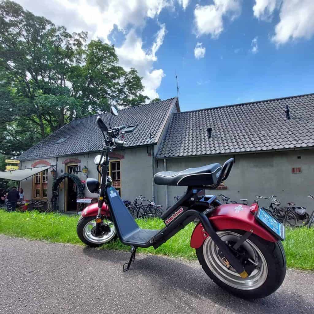 Elektrische scooter op 't Gelders Eiland met historische gebouwen op de achtergrond.