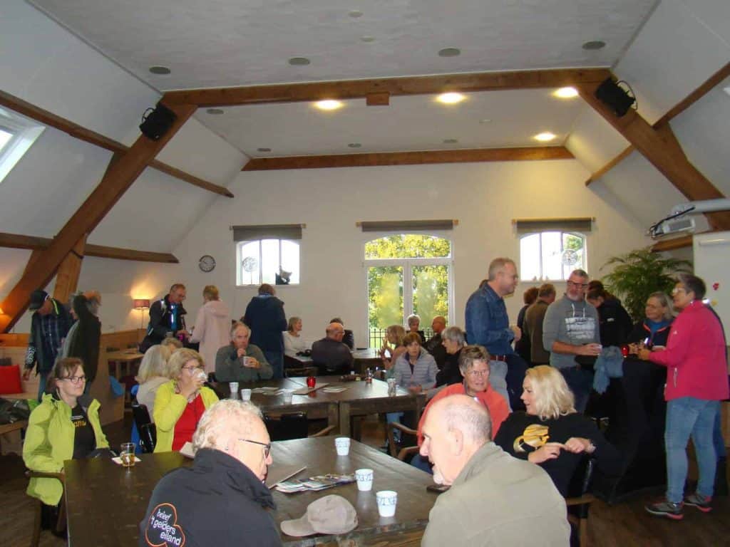 Gezellige bijeenkomst in een ruime zaal op 't Gelders Eiland met diverse mensen die praten en geniet.