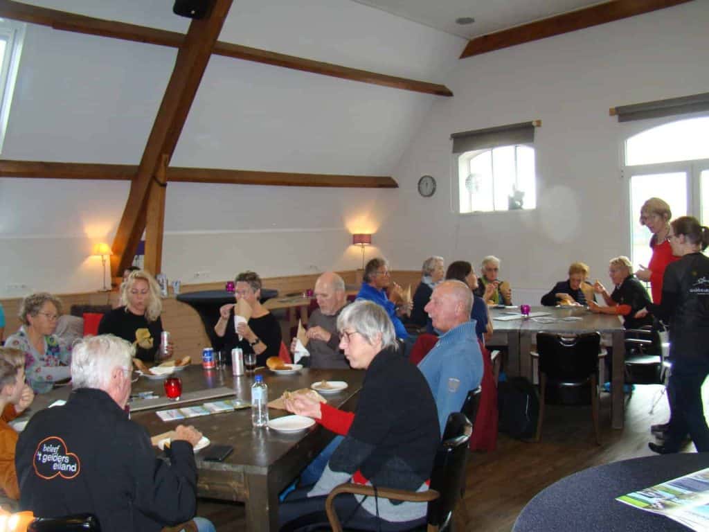 Gezellige groep ouderen geniet van een maaltijd in een sfeervolle zaal op 't Gelders Eiland.