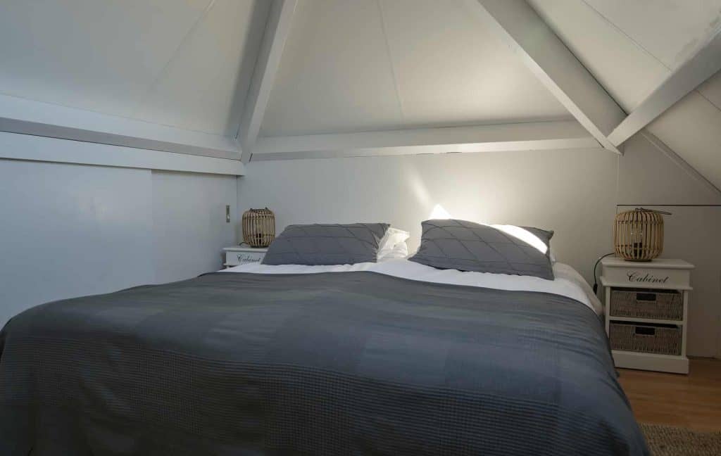 Huis in 't Gelders Eiland met slaapkamer onder schuine kap, lichte muren en moderne inrichting.