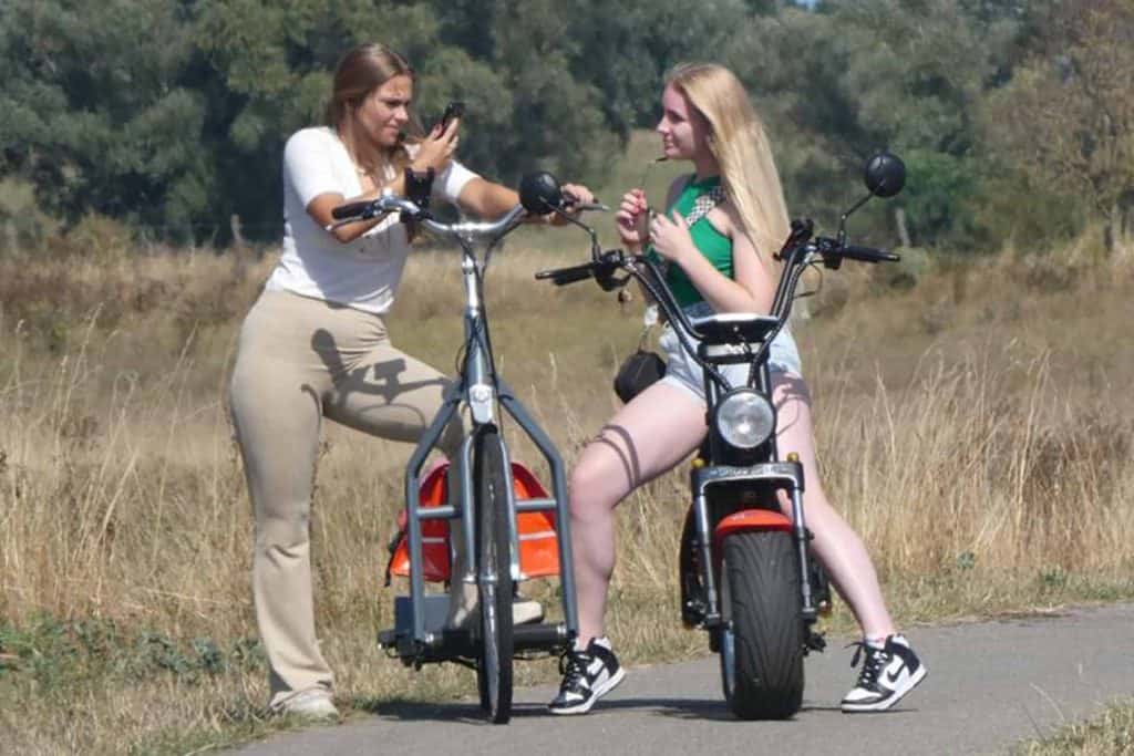 Twee jonge vrouwen met elektrische fiets en scooter op 't Gelders Eiland, genieten van de natuur.