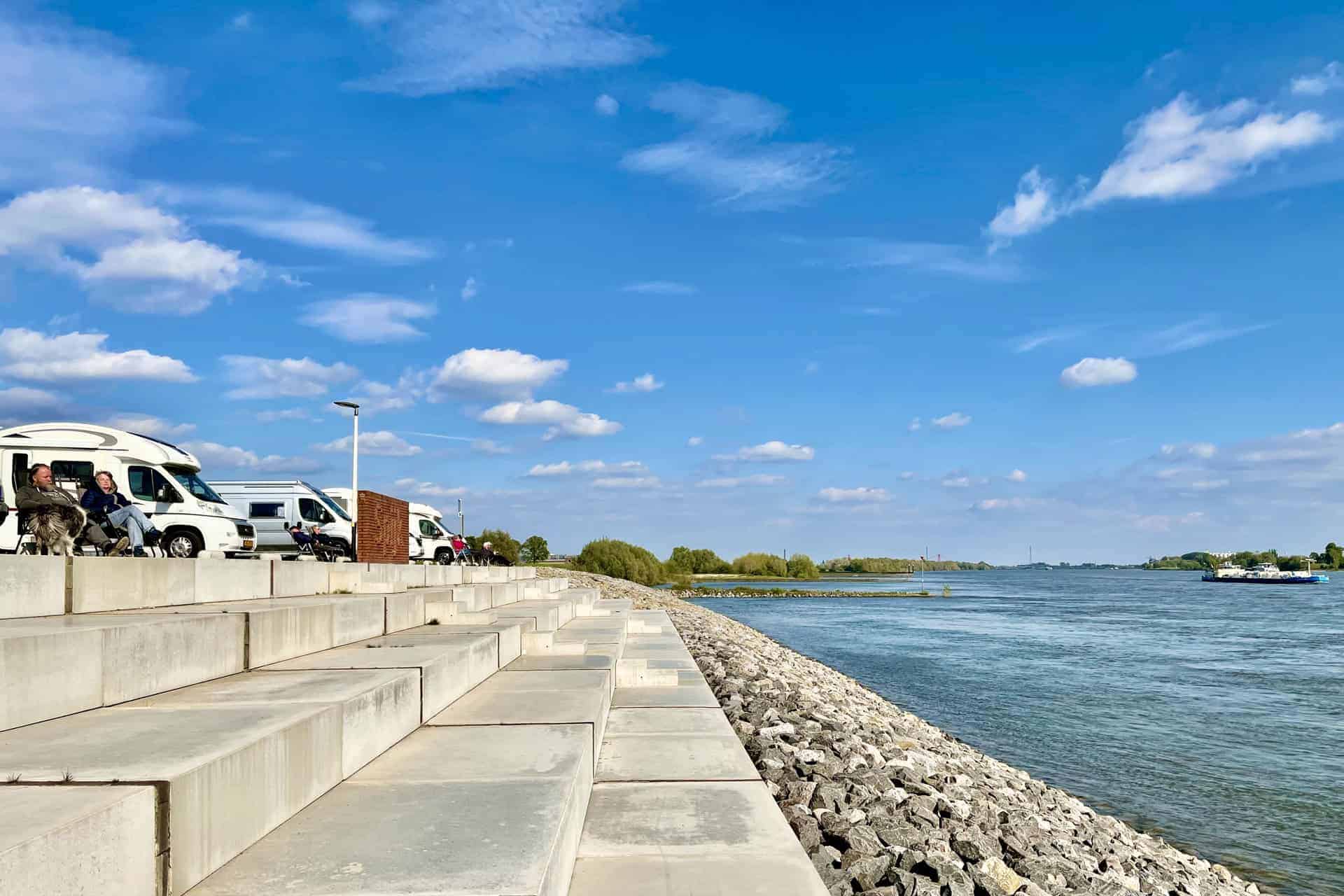 Gezicht op de rivier en de kade op 't Gelders Eiland, met blauwe lucht en wolken, ideaal voor ontspa.