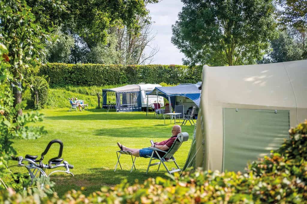 Kampeerplek met tenten en relaxende kampeerder op 't Gelders Eiland.