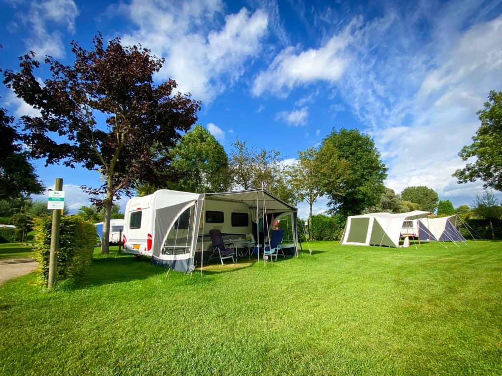 Kampeerplaatsen met tenten en caravans op 't Gelders Eiland, groene omgeving en blauwe lucht.