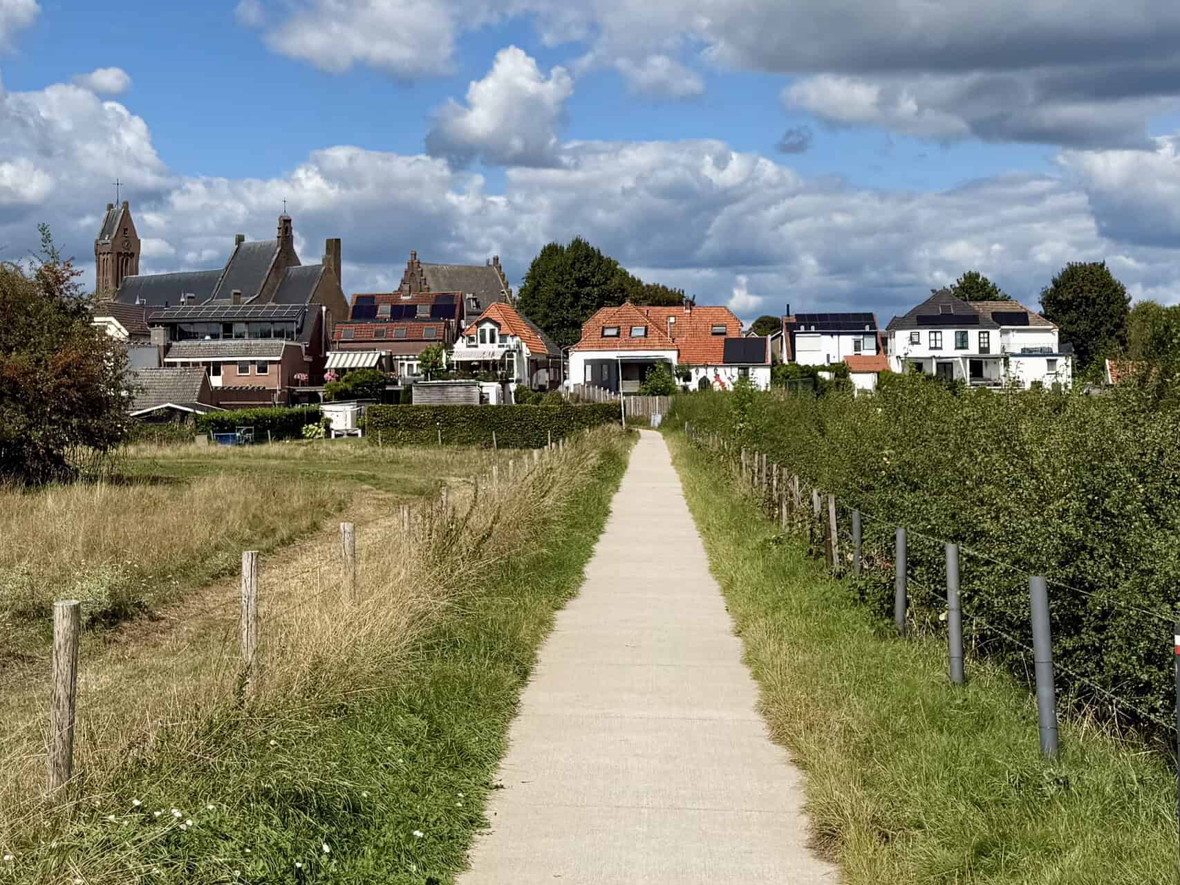 Gezicht op een dorp op 't Gelders Eiland met huizen en een kerk, onder een partly bewolkte hemel.