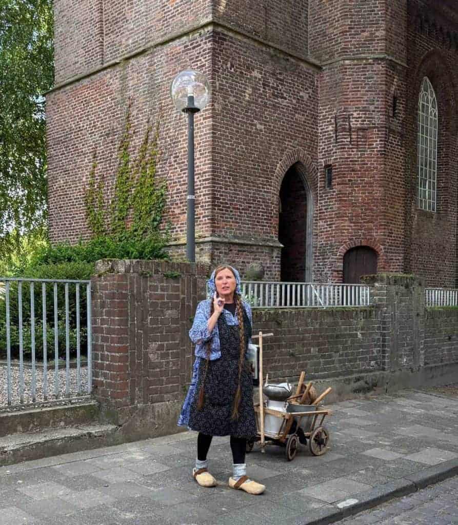 Een vrouw in historische kleding op 't Gelders Eiland met een handkar voor een oude kerk.