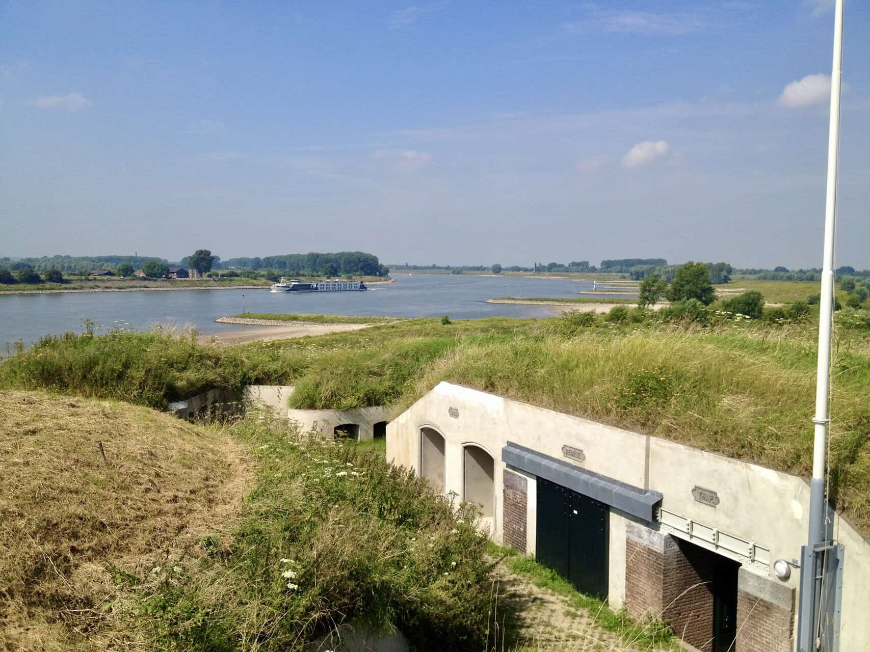 Zicht op de rivier en groene oevers op 't Gelders Eiland met historische waterwerken.
