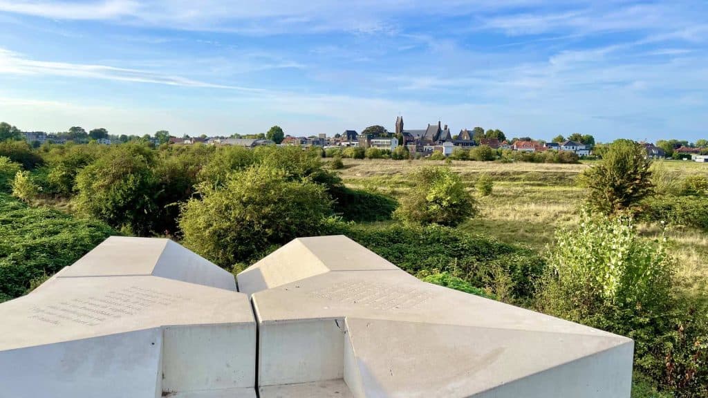 Zicht op 't Gelders Eiland met groene velden en een dorp in de verte onder een blauwe hemel.