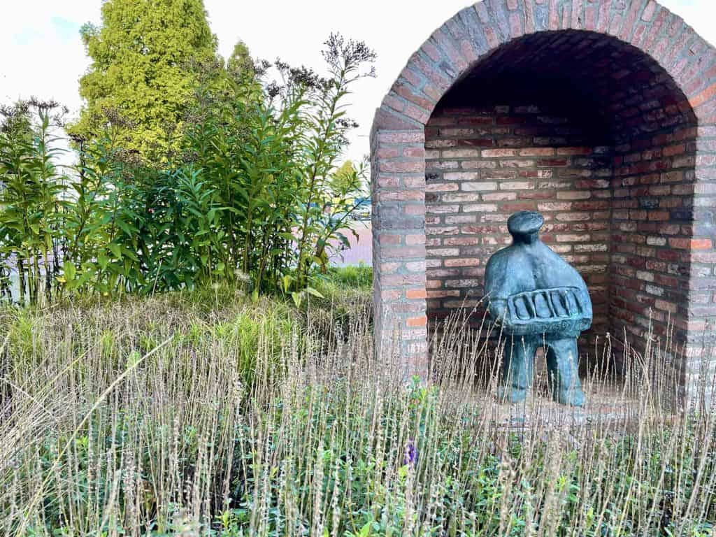 Houten beeld onder een boog van bakstenen op 't Gelders Eiland, omgeven door gras en groen.