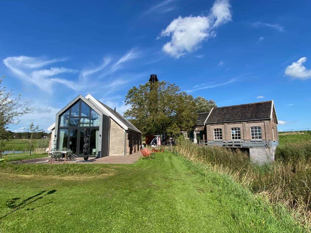 Modern glazen huis op 't Gelders Eiland met uitzicht op de natuur en blauwe hemel.