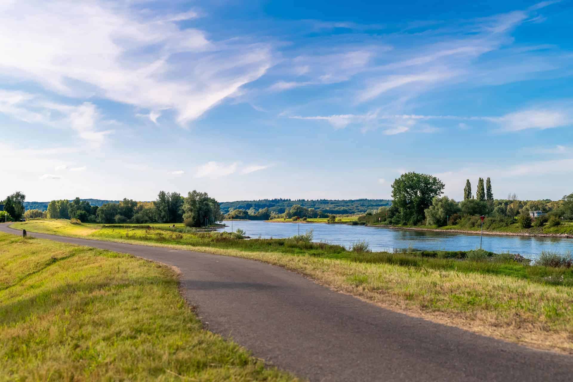 Gezicht op de rivier en groene velden op 't Gelders Eiland onder een blauwe hemel.
