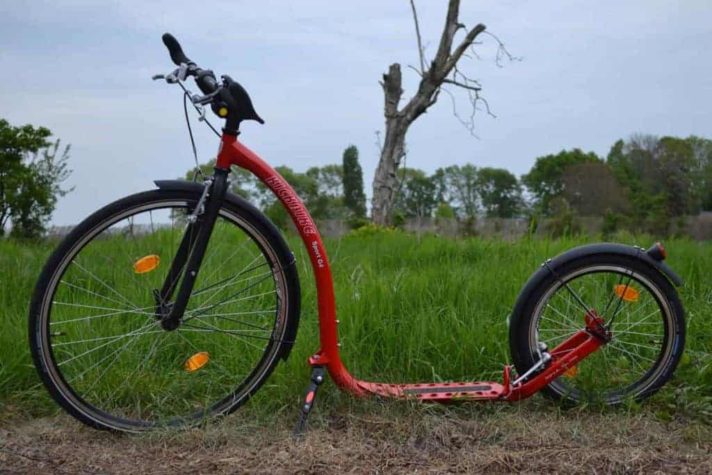 Rode elektrische scooter op grasland met bomen en blauwe lucht op 't Gelders Eiland.