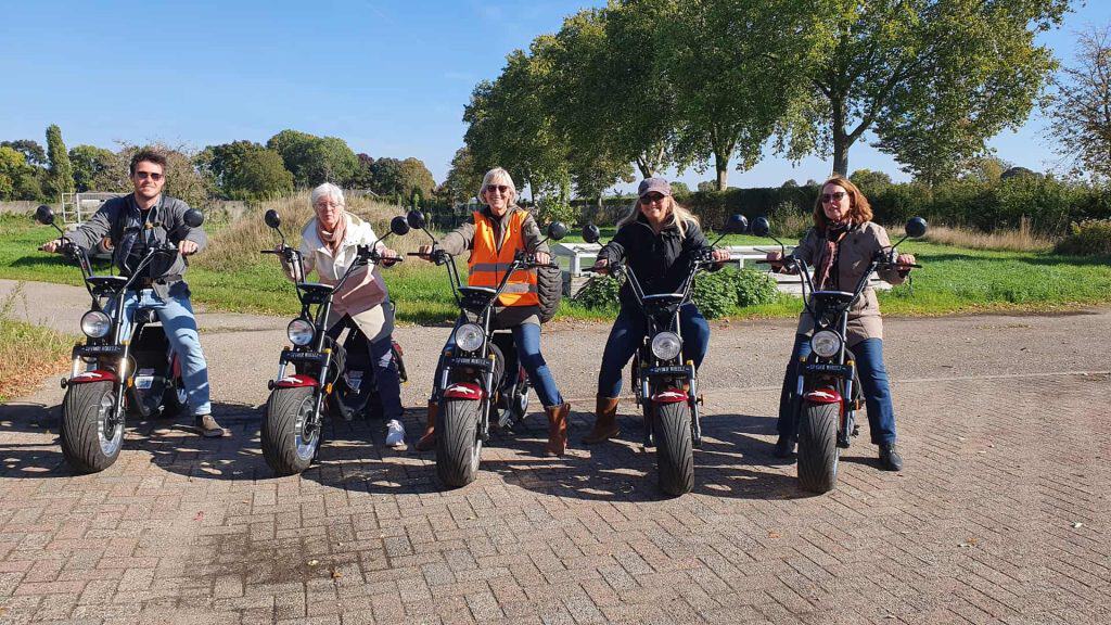 Groepsfoto van vijf mensen op elektrische scooters op 't Gelders Eiland, genieten van de natuur en h.