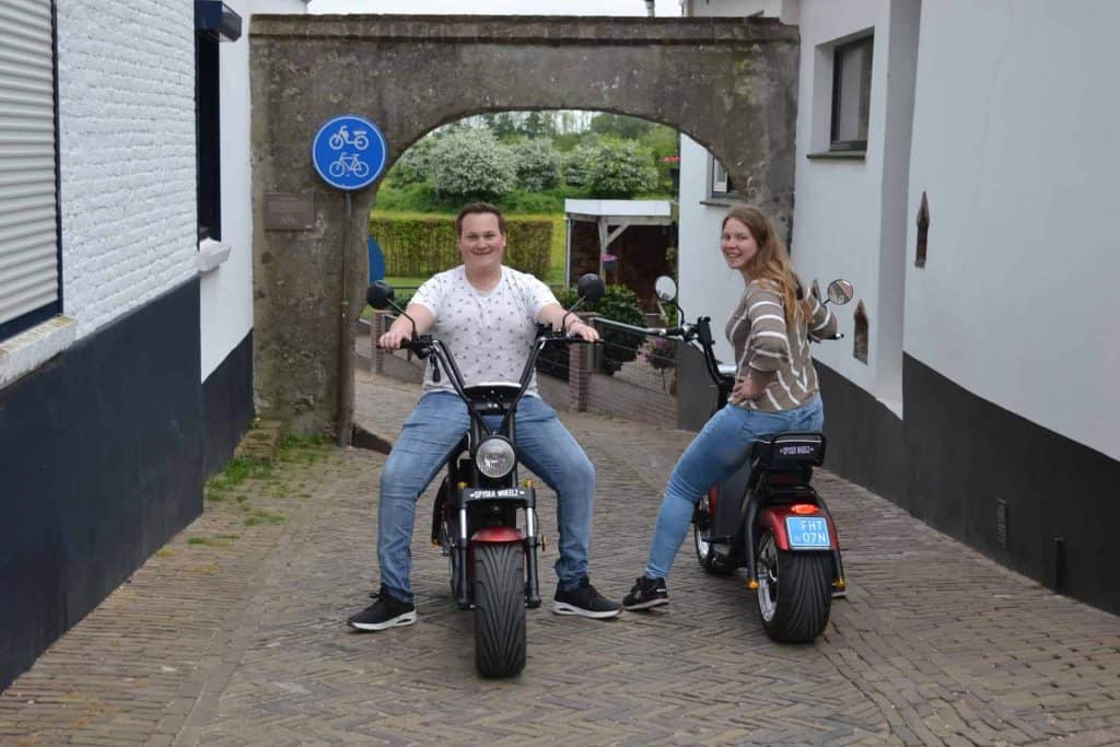 Twee jonge mensen op elektrische fietsen onder een historische poort op 't Gelders Eiland.
