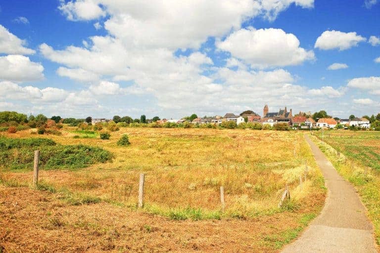 Uitzicht op het landschap van 't Gelders Eiland met wandelpad en dorp op de achtergrond.