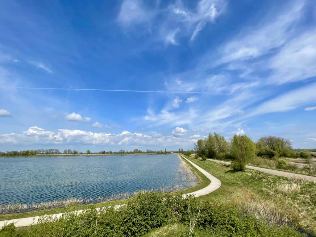 Uitzicht op 't Gelders Eiland met water, wandelpaden en groene natuur onder een heldere blauwe hemel.