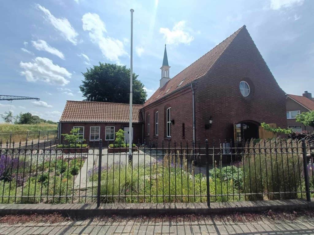 Kerk op 't Gelders Eiland met tuin en omheining, onder een blauwe hemel met wolken.