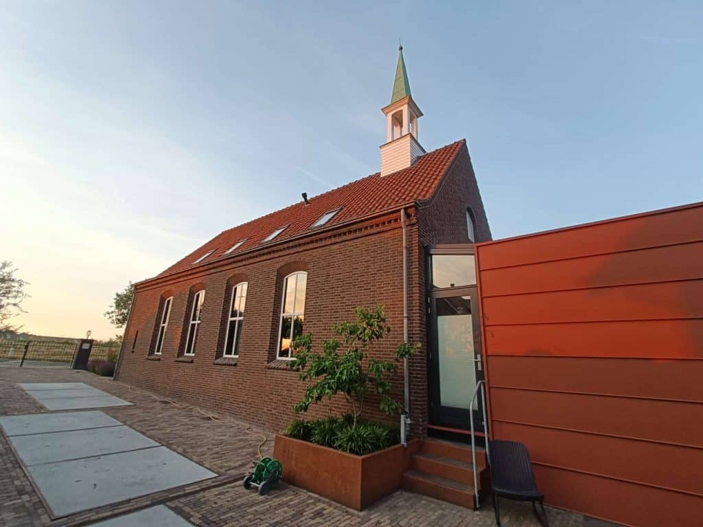 Kerk op 't Gelders Eiland met moderne uitbreiding en tuin, onder een heldere blauwe hemel.