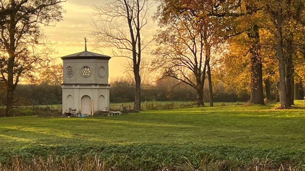 Kleine witte toren op 't Gelders Eiland met herfstbomen en zonsondergang op de achtergrond.