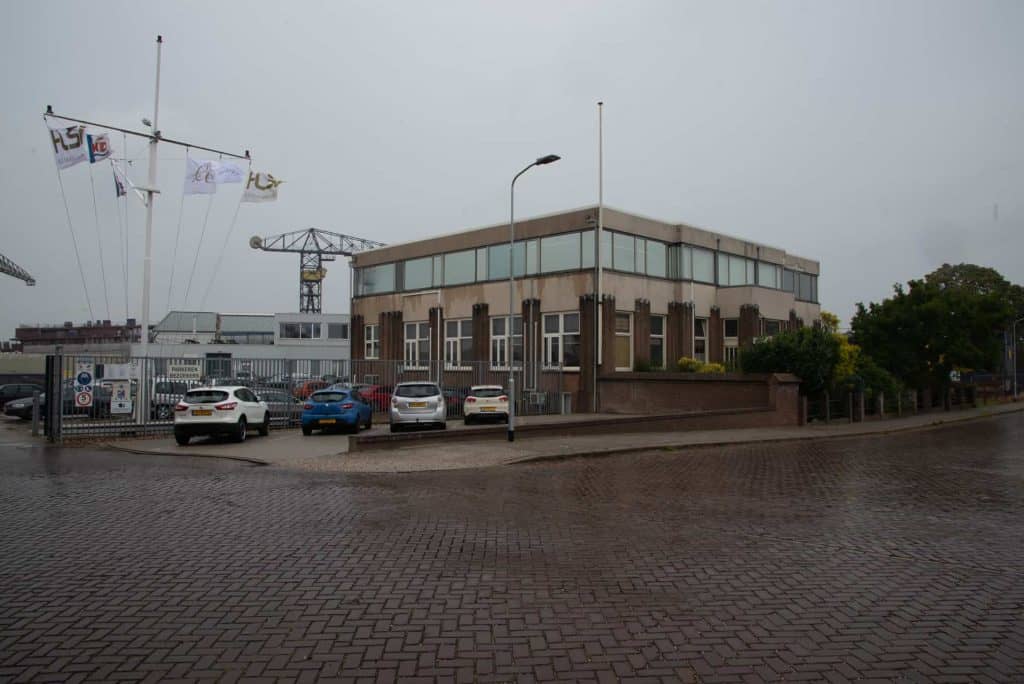 Kantoorgebouw op 't Gelders Eiland met parkeergelegenheid en vlaggen, onder een bewolkte hemel.