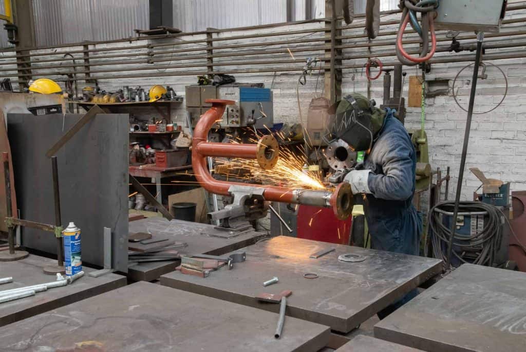 Lasergesneden metalen onderdeel in een werkplaats met een werknemer die beschermende uitrusting draa.