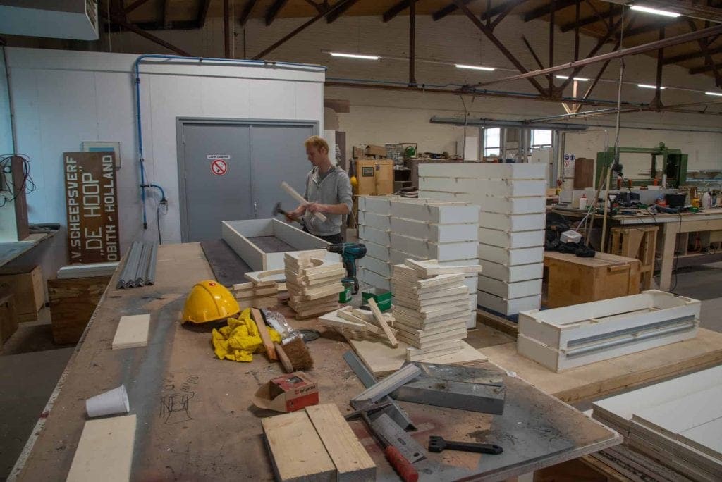 Houtbewerking in een werkplaats met stapels isolatiemateriaal en gereedschap.