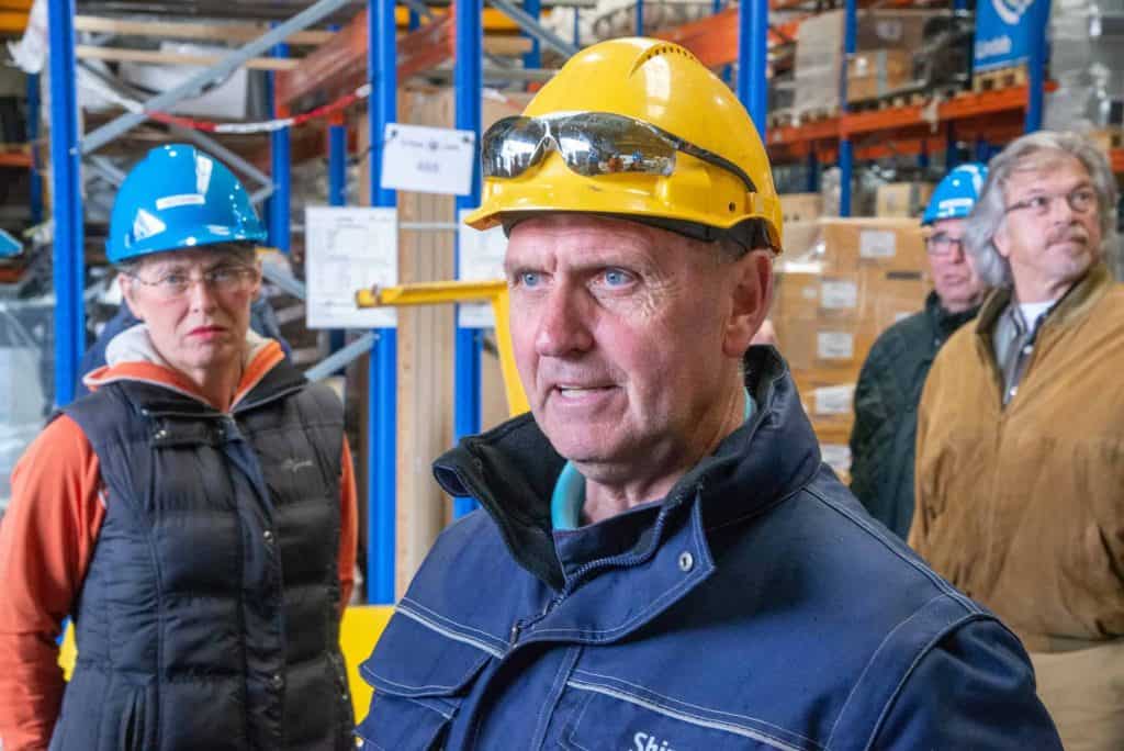 Veiligheidsinspectie in een magazijn met werknemers in beschermhelmen en veiligheidskleding.