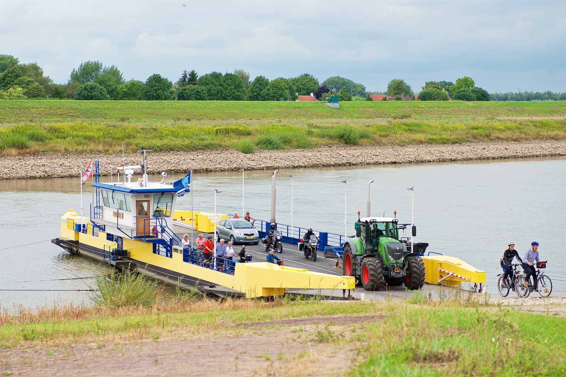 Veerpont met auto, fietsers en tractor op rivier bij 't Gelders Eiland.