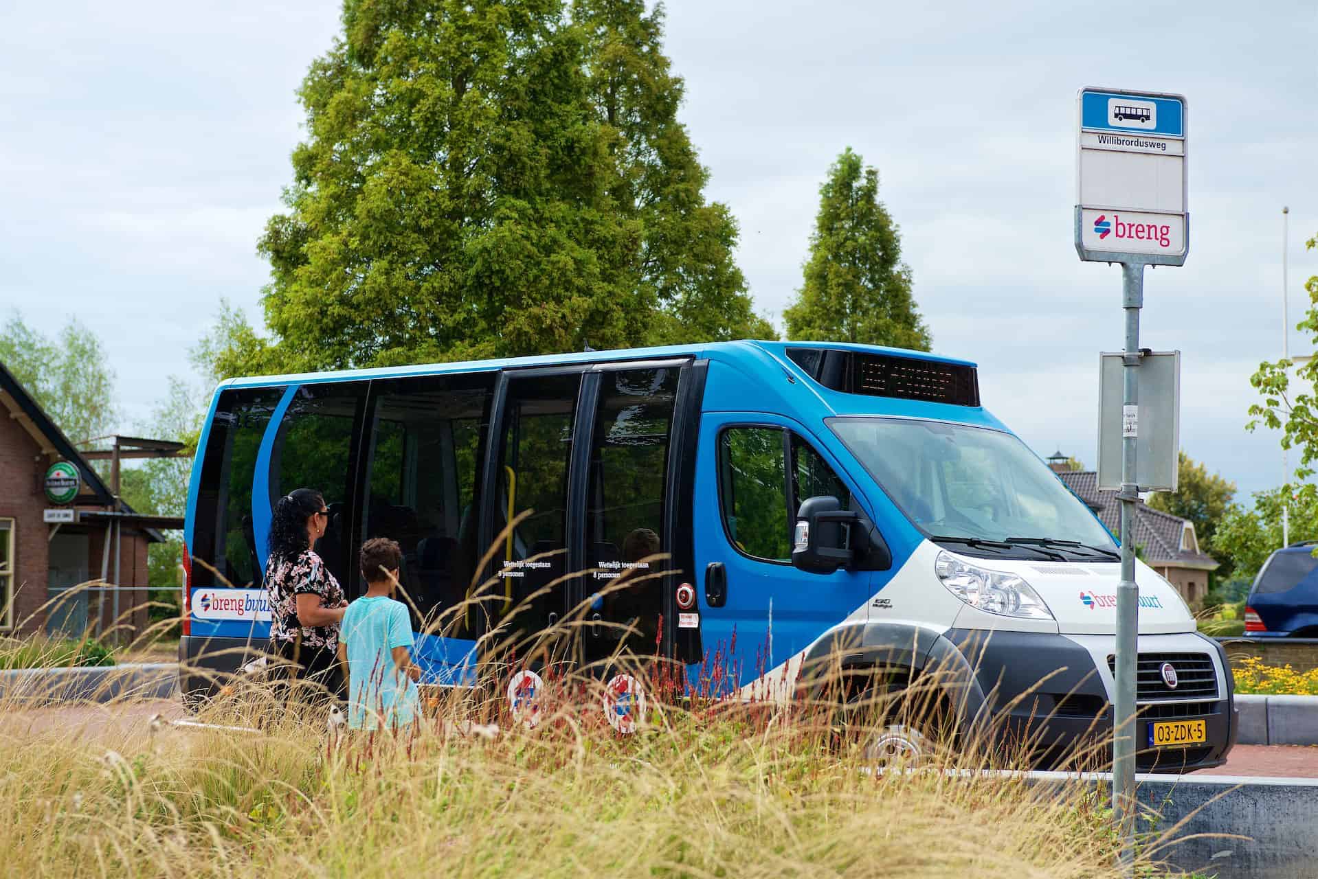 Blauwe bus op 't Gelders Eiland bij halte met reizigers.