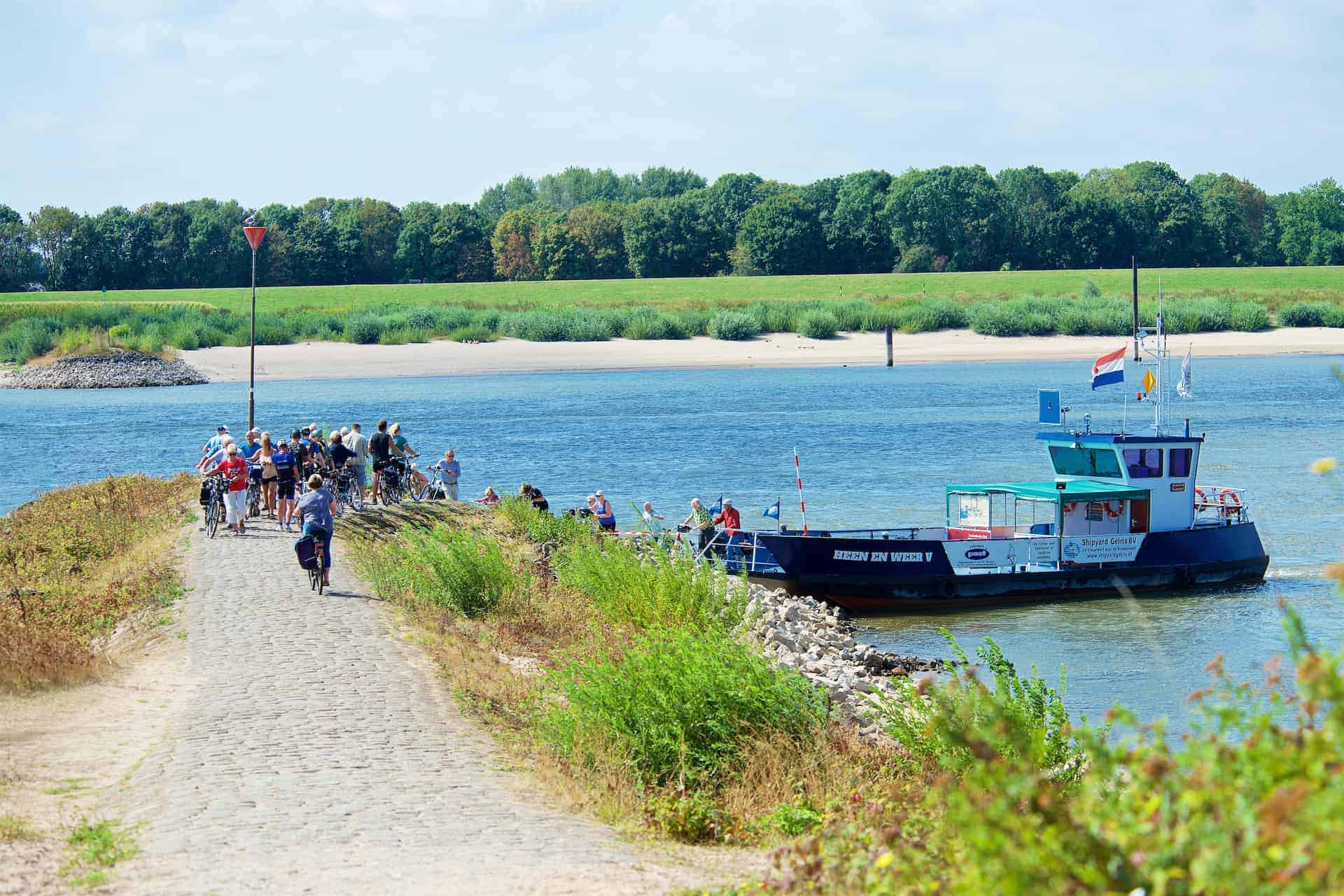 Wandelaars en boot op Gelders Eiland, rivier en groene omgeving.