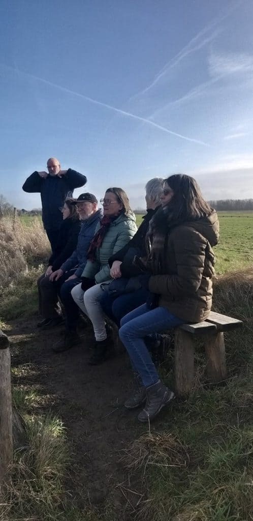 Gezelschap zit op bankje in natuur op 't Gelders Eiland, genieten van buitenlucht en landschap.