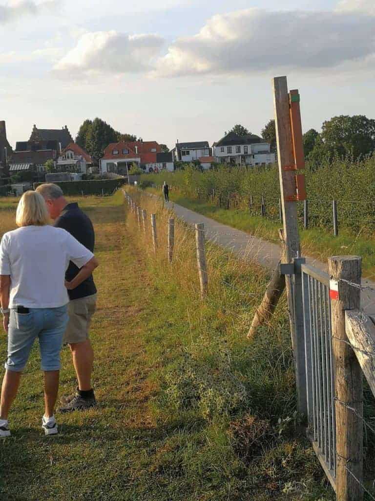 Wandelaars op het pad langs 't Gelders Eiland met uitzicht op huizen en natuur.