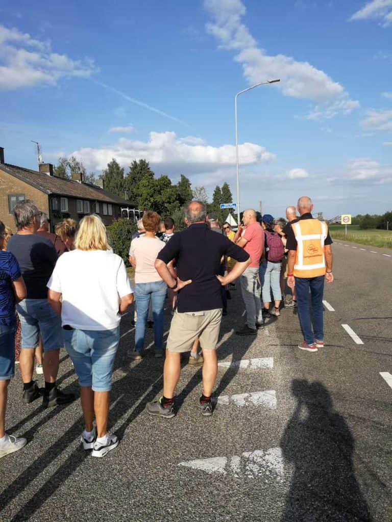Groep mensen wacht bij zebrapad op 't Gelders Eiland onder een blauwe hemel.