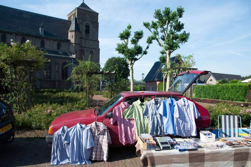 Kleding en spullen uitgestald op een markt op 't Gelders Eiland, met historische kerk op de achtergr.
