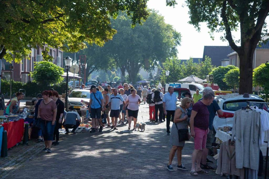 Gezellige markt op 't Gelders Eiland met bezoekers en kraampjes in de schaduw van bomen.