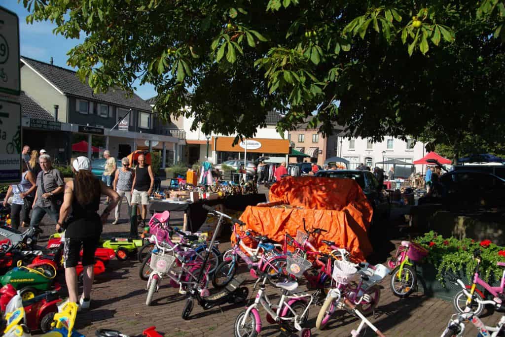 Een levendige markt op 't Gelders Eiland met kinderfietsen en bezoekers in de zon.