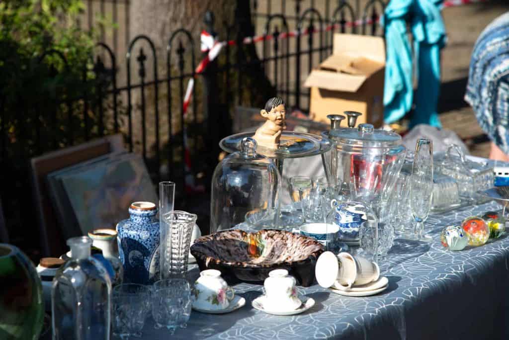 Kleine jongen speelt met water op een markt op 't Gelders Eiland, omringd door glazen en serviesgoed.