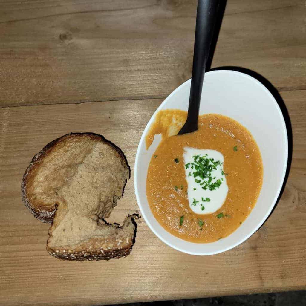 Romige tomatensoep met room en verse kruiden, geserveerd met knapperig brood op houten tafel.