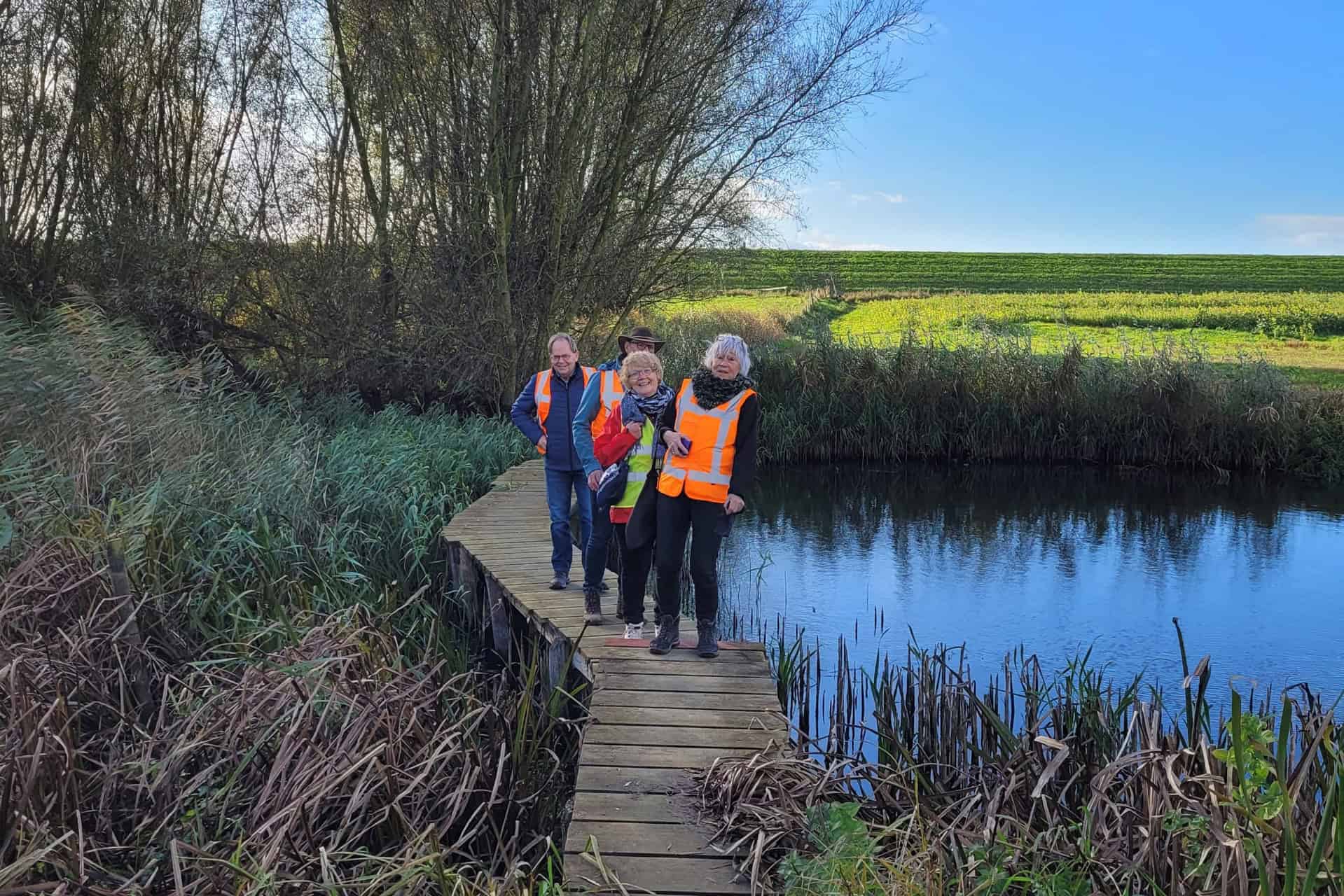 Drie mensen wandelen langs een waterkant op 't Gelders Eiland in de natuur.