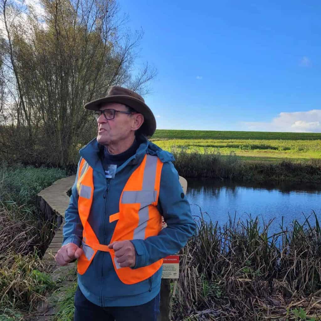 Landschap op 't Gelders Eiland met wandelaar in oranje veiligheidsvest, natuur en water.