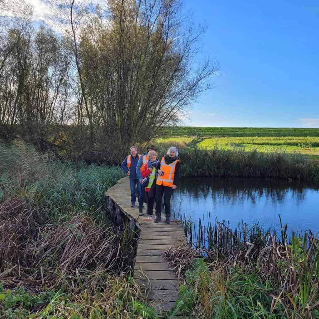 Veilig wandelen op 't Gelders Eiland langs een kleine waterkant met vier mensen in oranje veiligheid.
