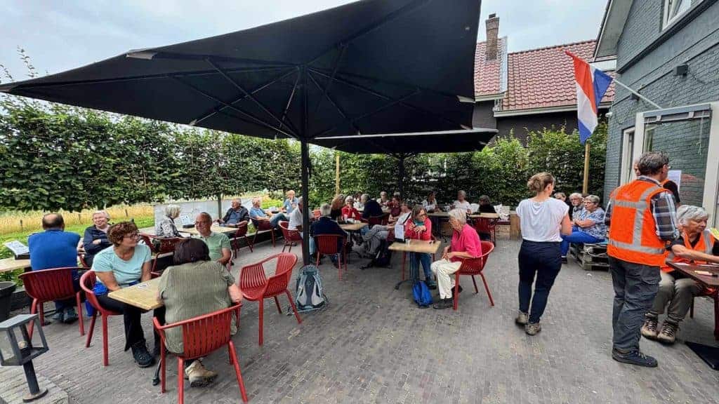 Gezellige terras met mensen op 't Gelders Eiland, onder een grote parasol, genietend van een ontspan.