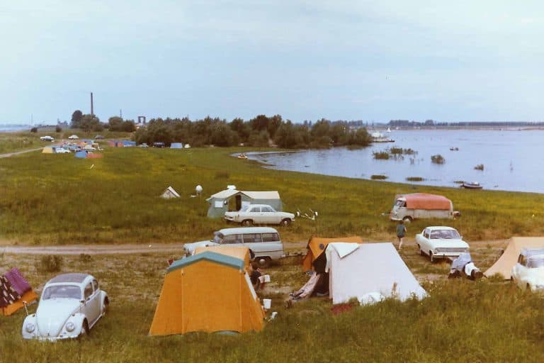 Gezicht op kampeerplaatsen met tenten en campers langs de rivier op 't Gelders Eiland.