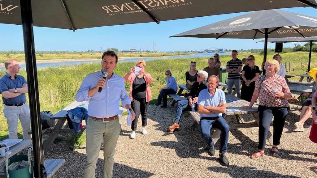 Groep mensen bij een buitenbijeenkomst op 't Gelders Eiland onder parasols.