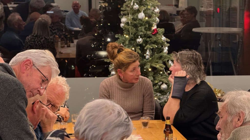 Gezellige bijeenkomst met ouderen rondom kerstboom tijdens jaarafsluiting TIC 2025.