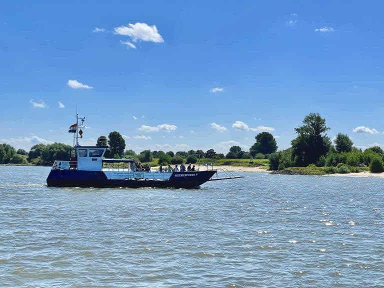 Vaarboot op de rivier met groene oevers en blauwe lucht.